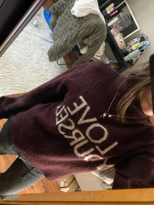 Vinröd stickad tröja med text - Mysig vinröd stickad tröja med hög krage och vit texten 'LOVE YOURSELF' framtill. Tröjan har en avslappnad passform och långa ärmar, perfekt för kalla dagar. Passar till jeans eller kjol för en trendig look.