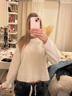 Vit stickad tröja med pärlor H&M - Säljer en vit stickad tröja från H&M med dekorativa pärlor på framsidan. Tröjan har en rak passform, ribbade muddar och en något högre rund halsringning. Perfekt för dig som gillar en enkel men ändå söt look.