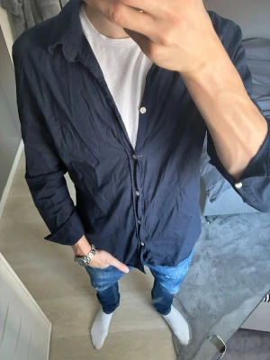 Mörkblå skjorta från Zara - Snygg mörkblå skjorta med klassisk krage och vita knappar. Skjortan är långärmad och har en avslappnad passform, perfekt att bära över en t-shirt. Tillverkad i mjuk bomull för en bekväm känsla.