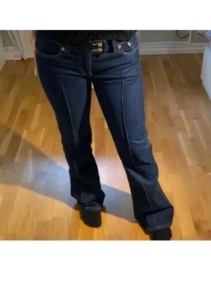Mörkblå bootcut jeans med kontrastsömmar - Säljer ett par mörkblå bootcut jeans med vita kontrastsömmar och pressveck framtill. Jeansen har låg midja och klassisk femficksmodell. Perfekta för dig som gillar retrovibbar och vill ha ett par jeans som sticker ut. Lånade bilder!