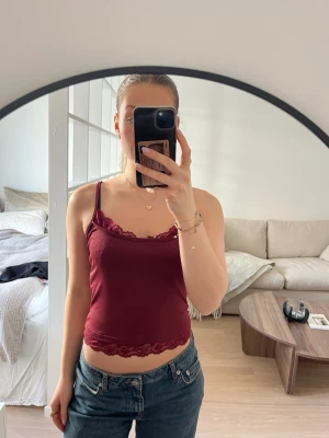 Vinröd  linnetopp - En vinröd linnetopp med tunna axelband och fina spetsdetaljer vid halsringning och nederkant. Toppen är lite croppad och har justerbara axelband. Aldrig använts.