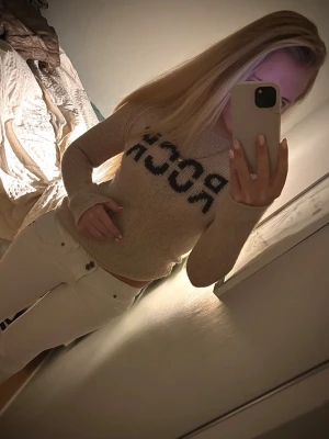 Beige stickad tröja från Zadig Voltaire med text  - Säljer en beige stickad tröja med svart text 'ROCK' framtill. Tröjan har långärmad design och rund hals. Perfekt för dig som gillar en enkel men cool stil. Passar till jeans eller kjol för en avslappnad look.