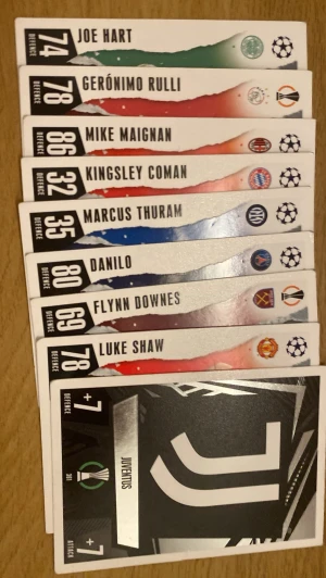 Match Attax fotbollssamlarbilder - Ett set med Match Attax samlarkort med fotbollstema. Korten har färgstarka designer och visar spelare som Joe Hart, Mike Maignan och Luke Shaw samt ett Juventus-kort. Perfekt för dig som gillar fotboll och att samla på kort.