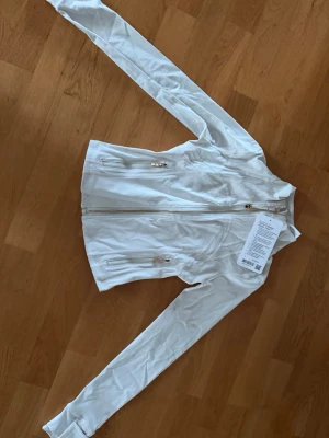 vit lululemon define jacket med guldiga detaljet - Tröjan är äkta och kommer med prislapp och i påse, jag säljer då den var för liten och då jag var lite osäker på passformen. Storlek 2 vilket motsvarar kring XS! Jag är också intresserad av att byta den mot en längre modell i en lite större storlek 🥰 Priset går att diskutera!