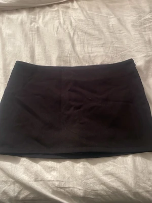 Svart kortkjol i bomull - Enkel och stilren svart kortkjol i kostym tyg. Kjolen har en rak passform och är perfekt att matcha med olika toppar för en clean look. Inga synliga detaljer eller mönster, bara klassisk och tidlös design.