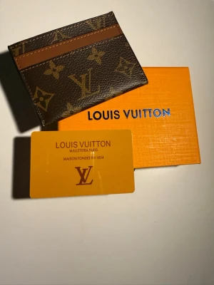 Louis Vuitton brun korthållare - Säljer en snygg korthållare från Louis Vuitton i klassiskt monogrammönster. Färgen är brun med ljusbruna detaljer och LV-logga över hela. Tillverkad i skinn och levereras med originalask och certifikat. Perfekt för dig som vill ha stilren och lyxig accessoar.