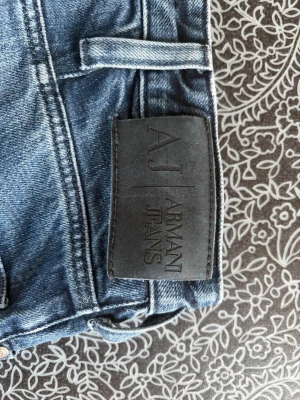Blå raka jeans från Armani Jeans - Säljer ett par klassiska blå jeans från Armani Jeans med rak passform och fem fickor. Jeansen har en snygg tvättad look och är tillverkade i slitstarkt denimtyg. Perfekta för en avslappnad och stilren outfit.