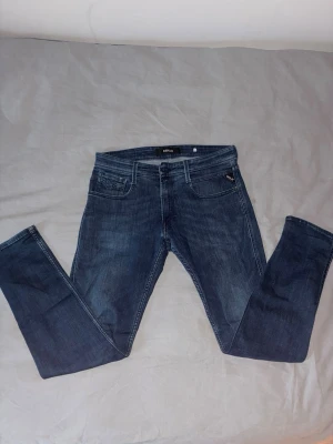 Mörkblå Replay jeans slim fit - Säljer ett par mörkblå slim fit jeans från Replay med klassisk femficksdesign och dragkedja. Jeansen har snygga slitningar och raka ben. Perfekta för dig som gillar en stilren look. Mitt pris (449kr) nypris (1200kr)