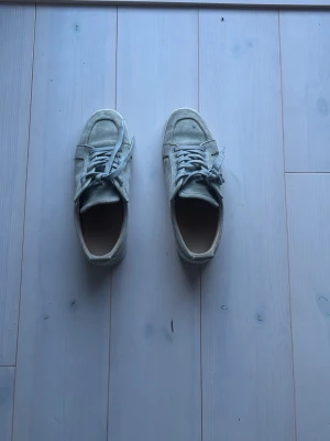 Ljusgråa loubs i mocka - Säljer ett par ljusgråa loubs i mocka med klassisk låg profil och vita snören. Skorna har en enkel och stilren design med rund tå och diskreta sömmar. Passar perfekt till streetwear och casual outfits. 