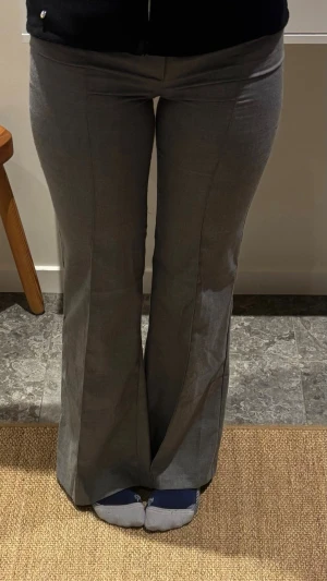 Grå kostymbyxor med utsvängda ben - Snygga grå kostymbyxor med pressveck och utsvängda ben. Byxorna har låg midja och stängs med dold dragkedja framtill. Aldrig använda och säljs pga de är för små.