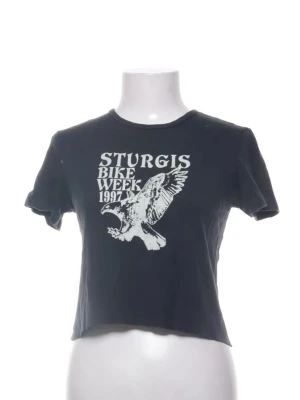 Svart t-shirt - Svart croppad t-shirt från John golt med coolt vintage-tryck framtill: 'Sturgis Bike Week 1997' och en stor örn. T-shirten har korta ärmar, rund hals och är gjord i mjuk bomull. Perfekt för dig som gillar retro vibes och statement-plagg.