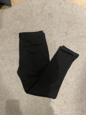 Svarta slim fit kostymbyxor - Snygga svarta kostymbyxor i slim fit-modell med pressveck och bälteshällor. Byxorna har två sidofickor fram och en diskret bakficka. Perfekta för en clean och stilren look. Materialet känns mjukt och följsamt.