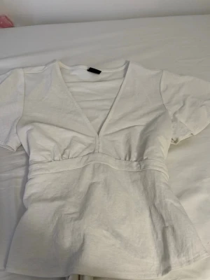 Vit v-ringad topp från Gina Tricot - Säljer en vit topp från Gina Tricot i mjuk bomull. Toppen har korta ärmar, markerad midja och en djup v-ringning framtill. Enkel och stilren design som passar perfekt till jeans eller kjol.