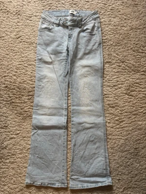Ljusblå bootcut jeans med låg midja - Säljer ett par ljusblå bootcut jeans med låg midja och dubbla knappar i linningen. Jeansen har klassiska fem fickor och är tillverkade i denim med en lätt tvättad look. Nypris 400kr.