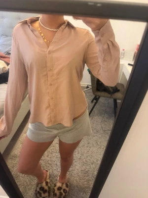 Beige rosa satinblus med krage - Snygg beige blus i satinliknande material med klassisk krage och knäppning framtill. Blusen har långa ärmar och en avslappnad passform som ger en stilren och trendig look. Perfekt att styla med jeans eller kjol för en chic vibe.