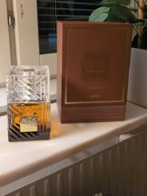 Säljer/byter - Säljer/ byter Lattafa Khamrah Qahwa Eau de Parfum i en lyxig, fyrkantig glasflaska med detaljerad slipning och guldplakett. Flaskan har en brun tonad botten och transparent lock. Kommer i elegant brun och guld kartong. Volym: 100 ml.