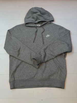 Grå hoodie från Nike med logga. Pris kan sänkas!!! - Snygg grå hoodie från Nike med klassisk vit logga på bröstet. Hoodien har huva med dragsko och en mjuk insida. Perfekt för en avslappnad och sportig stil. Ribbade muddar vid ärmslut och nederkant.