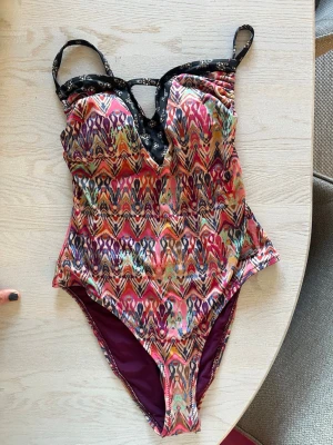Ny ODD MOLLY Baddräkt, swimsuit strl 0 - Säljer en ny ODD MOLLY baddräkt storlek 0 (xs) (34) med färgstarkt etnoinspirerat mönster i rosa, lila, orange och grönt. Svarta axelband med vita blommor och snygg cut-out framtill. Insidan är vinröd och baddräkten har vadderade kupor för extra stöd. Perfekt för stranden eller poolen!