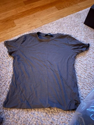 Två basic t-shirts i grått och vitt - Två enkla t-shirts i klassisk modell, en i grått och en i vitt. Båda har rund halsringning och korta ärmar. Perfekta att matcha med jeans eller shorts för en avslappnad stil.