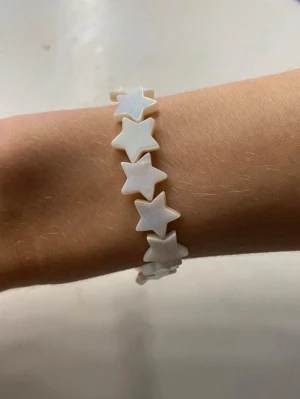 Vitt armband med stjärnpärlor - Superfint armband med vita pärlor formade som stjärnor. Pärlorna har en lätt skimrande yta och sitter på en elastisk tråd, vilket gör det enkelt att ta på och av. Perfekt accessoar för att ge din stil en lekfull touch.