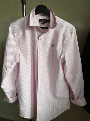 Rosa och vit randig skjorta Polo Ralph Lauren - Riktigt fräsch skjorta från Ralph Lauren i nyskick, storlek M, mått kan lösas om så är. Ärmarna är uppkavlade på bild.