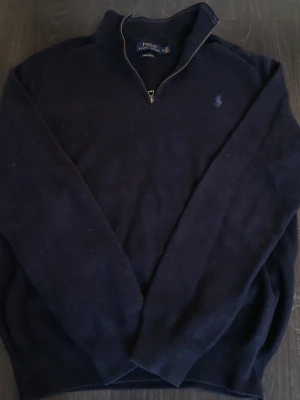 Mörkblå quarter zip tröja Polo Ralph Lauren - Mörkblå långärmad tröja från Polo Ralph Lauren med quarter zip och broderad logga på bröstet. Tröjan är stickad och har en klassisk passform med hög krage. Perfekt för lager-på-lager och chill höst- och vinterstil. Axelbredd: 45cm / Längd: 60cm. Nypris: 2599kr / Mitt pris: 649kr