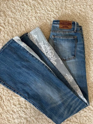 Blå bootcut jeans med spetsdetaljer - Unika blå bootcut jeans från Crocker. Stl 27/33 (xs). Mått rakt över midjan: 33 cm. Passar mig som är 166 cm lång.