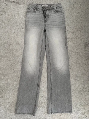 Grå raka jeans från Pull&Bear - Snygga grå jeans från Pull&Bear med raka ben och klassisk femficksdesign. Jeansen har en ljus tvätt med slitna detaljer och rå kant nedtill. Tillverkade i denim med en cool vintagekänsla. Perfekta för en avslappnad och trendig look.