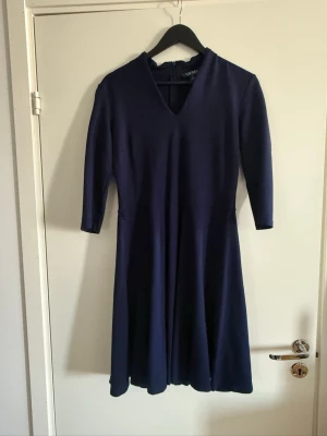 Mörkblå klänning från Lauren Ralph Lauren - Mörkblå klänning från Lauren Ralph Lauren med v-ringning och trekvartsärm. Klänningen har en elegant, enkel design och dragkedja i ryggen. Perfekt för dig som gillar klassisk stil och vill ha något stilrent i garderoben.