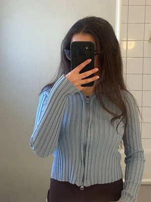 Ljusblå ribbad ziptröja från Nakd - Säljer en ljusblå ribbad tröja med dragkedja framtill. Tröjan har lång ärm, figurnära passform och är tillverkad i ett stretchigt material. Perfekt för en trendig och avslappnad look. För fler bilder fråga