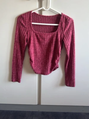 Ribbad rosa långärmad topp - Trendig ribbad topp i rosa med lång ärm och fyrkantig ringning. Perfekt för att styla med jeans eller kjol. Mjuk och stretchig känsla, passar dig som gillar en enkel men snygg look.