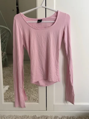 Ljusrosa långärmad topp - En enkel och stilren ljusrosa långärmad topp med rund halsringning. Tillverkad i mjukt bomullsmaterial som känns skönt mot huden. Perfekt att matcha med jeans eller kjol för en avslappnad look.