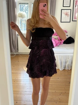 Jane Norman klänning - Säljer en kort axelbandslös klänning i svart och lila med volangdetaljer och glitter. Från Jane Norman, skulle säga storlek xs. Jättefint skick!💕