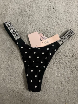 Svarta stringtrosor med prickar Victoria's Secret - !ALDRIG TESTADE!                                             Svarta stringtrosor från Victoria's Secret med vita prickar och glittriga resårband där märkesnamnet står. Storlek xs ❤️