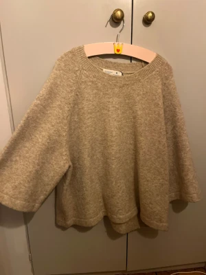 Beige stickad tröja  - Beige stickad tröja från primarket, med vid passform och trekvartsärmar. Tröjan har rund halsringning och är gjord i ett mjukt, ulligt material som känns riktigt cozy. Perfekt för lager-på-lager och chill höst- och vinterstil men även till lite kallare sommarkvällar.