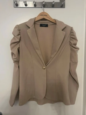 Beige kavaj med puffärmar Sisters Point - Stilren beige kavaj från Sisters Point med puffade ärmar och klassisk krage. Oanvänd utan prislapp.