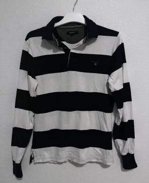 Randig pikétröja från GANT storlek XS - Snygg långärmad pikétröja från GANT i storlek XS. Tröjan har breda marinblå och vita ränder. Perfekt för dig som gillar att ha något som sticker ut.