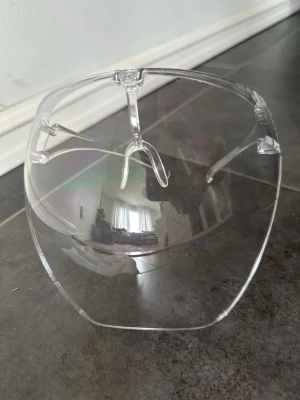 Transparenta futuristiska ansiktsskydd  - Säljer ett par unika, transparenta solglasögon med helskärm-design. Glasögonen har en modern och futuristisk look med rundad form och näsbrygga i plast. Perfekta för dig som vill sticka ut och ha en cool accessoar till sommaren.