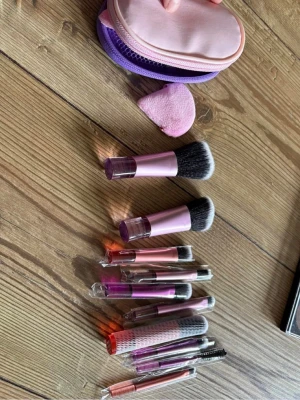 Rosa sminkborstset med väska travel kit  - Ett komplett sminkborstset med flera borstar i olika storlekar och former, perfekt för både bas, ögon och bryn. Borstarna har rosa och lila detaljer, syntetiska borst och medföljer en rosa och lila förvaringsväska samt en mjuk makeupsvamp. 10 stycken plus 1 powder puff. Helt oanvända 
