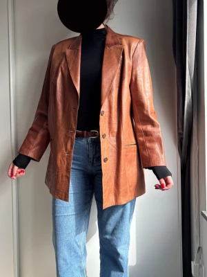 Brun oversized skinnjacka - Snygg brun oversized skinnjacka med klassisk krage och tre knappar framtill. Jackan har raka axlar, två fickor och en avslappnad passform som ger en cool vintagekänsla. Jackan är i äkta mjukt skinn och från en vintage butik. Skulle säga i storlek L!🤎