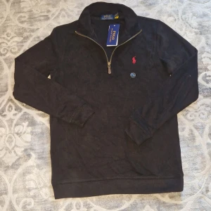 Polo Raplh Lauren half zip - Svart långärmad tröja från Polo Ralph Lauren med half zip och klassisk röd broderad logga på bröstet. Tröjan har hög krage och är tillverkad i mjuk bomull, perfekt för lager-på-lager. Enkel och stilren design som funkar till allt.