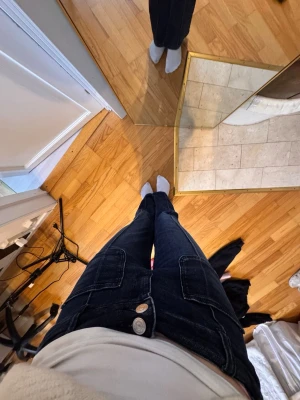 Mörkblå jeans med fickor fram - Säljer ett par mörkblå jeans med raka ben och stora fickor framtill. Jeansen har dubbla silverknappar i midjan och kontrastsömmar. Snygg och enkel modell som passar till det mesta. Materialet är klassisk denim.