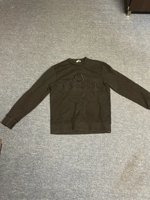 Svart sweatshirt från Moncler - Snygg svart sweatshirt från Moncler med broderad logga och text framtill. Tröjan har rund halsringning, långa ärmar och ribbade muddar vid ärmslut och nederkant. Perfekt för en stilren och avslappnad look.