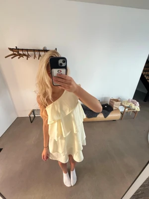 Ljusgul oneshoulder volangklänning - Söt ljusgul klänning med oneshoulder och flera volanglager. Klänningen har en luftig och flowy passform, perfekt för varma dagar. Materialet känns lätt och bekvämt mot huden. Enkel men ändå trendig design som sticker ut.