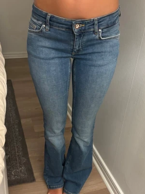 Blå bootcut jeans från ONLY - Säljer ett par klassiska blå bootcut jeans från ONLY med låg midja och femficksmodell. Jeansen har en snygg tvättad look och är tillverkade i stretchigt denimtyg för skön passform. Perfekta till sneakers eller boots! Storlek waist S och längd 32