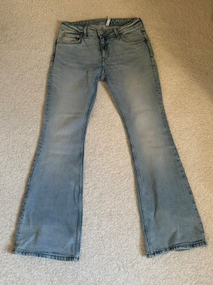 Ljusblå bootcut jeans från Weekday  - Säljer ett par ljusblå bootcut jeans med klassisk femficksmodell och utsvängda ben. Jeansen har en snygg tvättad look och är tillverkade i denim med en skön känsla. Perfekta för dig som gillar retrostil och vill ha ett par jeans som sticker ut. Finns svag tecken på slitage längst ner på benet men inga hål!
