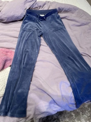 Blå velour mjukisbyxor Juicy Couture - Mysiga blå mjukisbyxor i velour från Juicy Couture. Byxorna har raka/baggy ben, resår och dragsko i midjan samt fickor både fram och bak. Perfekta för en chill och avslappnad stil.