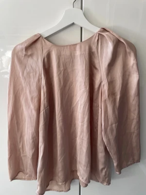 Beige blus från Gina Tricot - Säljer en beige blus från Gina Tricot med lös passform och rund halsringning. Blusen har långa ärmar och är tillverkad i ett tunt, glansigt material som ger ett elegant intryck. Perfekt att styla med jeans eller kjol för en trendig look.
