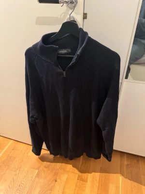 Mörkblå stickad halvziptröja - Mörkblå stickad tröja från Dressman med halv dragkedja och hög krage. Tröjan har en avslappnad passform och är tillverkad i mjukt material som passar perfekt för kyligare dagar. Klassisk och enkel design som funkar till det mesta.