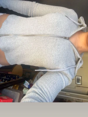 Ljusgrå ribbad hoodie med dragkedja - Säljer en ljusgrå ribbad hoodie med dragkedja framtill och snörning i huvan. Tröjan har en tight passform och långa ärmar. Perfekt för en chill och avslappnad stil.